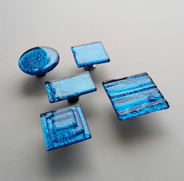 Fired glass cabinet knobs in sparkly deep blue made of round, square and rectangular glass pieces attached over a metal base. Slightly textured glass furniture handles with rounded edges.