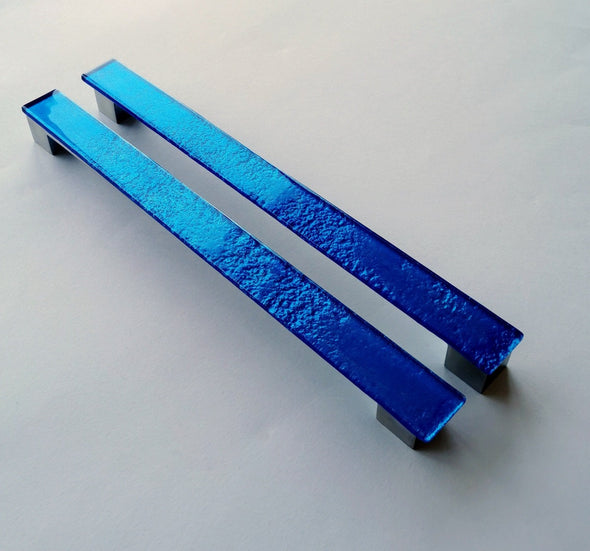 Set of two sparkly deep blue fired glass fridge pulls made of long glass sticks attached over a silvery metal base. Slightly textured glass furniture handles with rounded edges.