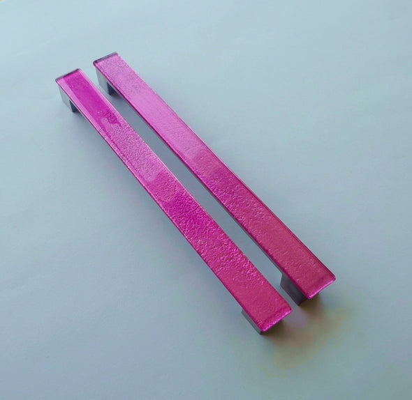 Set of two bright pink fired glass fridge pulls made of long glass sticks attached over a silvery metal base. Slightly textured glass furniture handles with rounded edges.
