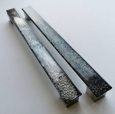Set of two sparkly bright black fired glass fridge pulls made of long glass sticks attached over a silvery metal base. Slightly textured glass furniture handles with rounded edges.