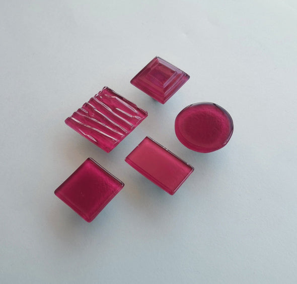 Fired glass cabinet knobs in matte deep red made of round, square and rectangular glass pieces attached over a metal base. Slightly textured glass furniture handles with rounded edges.