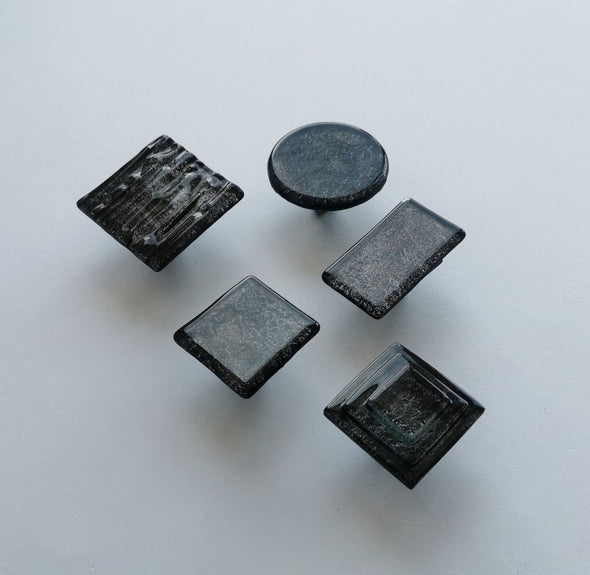 Fired glass cabinet knobs in sparkly bright black made of round, square and rectangular glass pieces attached over a metal base. Slightly textured glass furniture handles with rounded edges.