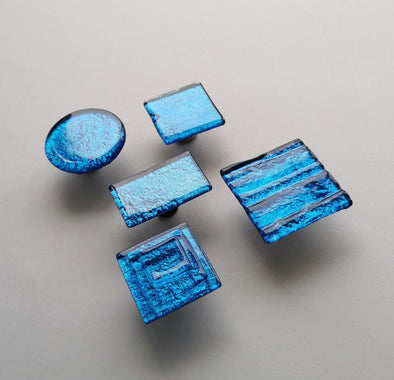 Fired glass cabinet knobs in sparkly deep blue made of round, square and rectangular glass pieces attached over a metal base. Slightly textured glass furniture handles with rounded edges.