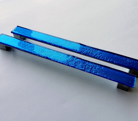 Set of two sparkly deep blue fired glass fridge pulls made of long glass sticks attached over a silvery metal base. Slightly textured glass furniture handles with rounded edges.