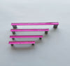 Fired glass cabinet pulls in bright pink made of fine glass sticks attached over a metal base. Slightly textured glass furniture handles with rounded edges.
