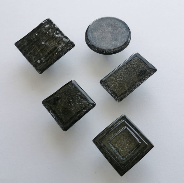 Fired glass cabinet knobs in sparkly bright black made of round, square and rectangular glass pieces attached over a metal base. Slightly textured glass furniture handles with rounded edges.