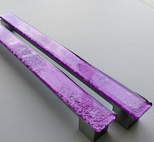 Set of two sparkly bright purple fired glass fridge pulls made of long glass sticks attached over a silvery metal base. Slightly textured glass furniture handles with rounded edges.